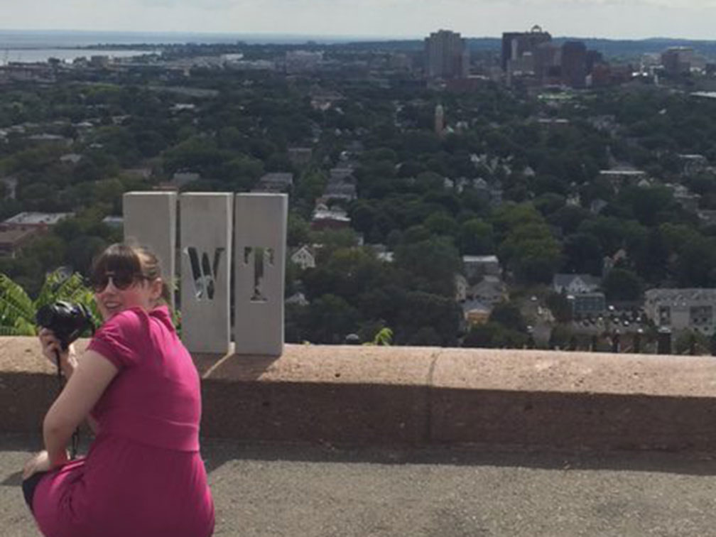woman in pink dress holding camera with city skyline in the distance